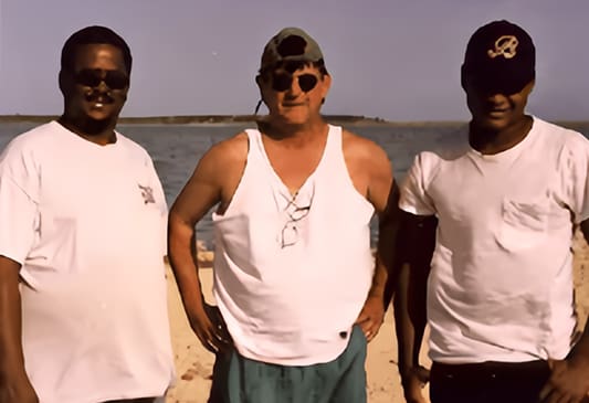 Three men standing on the beach in front of water.